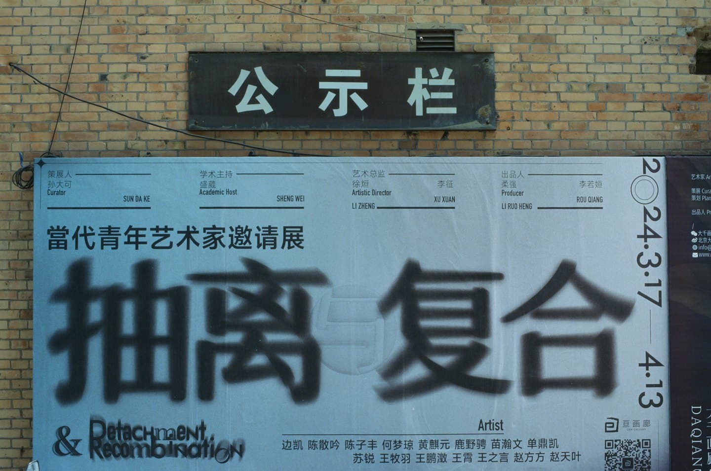Ausstellungsposter mit chinesischen Schriftzeichen an einer Ziegelwand.