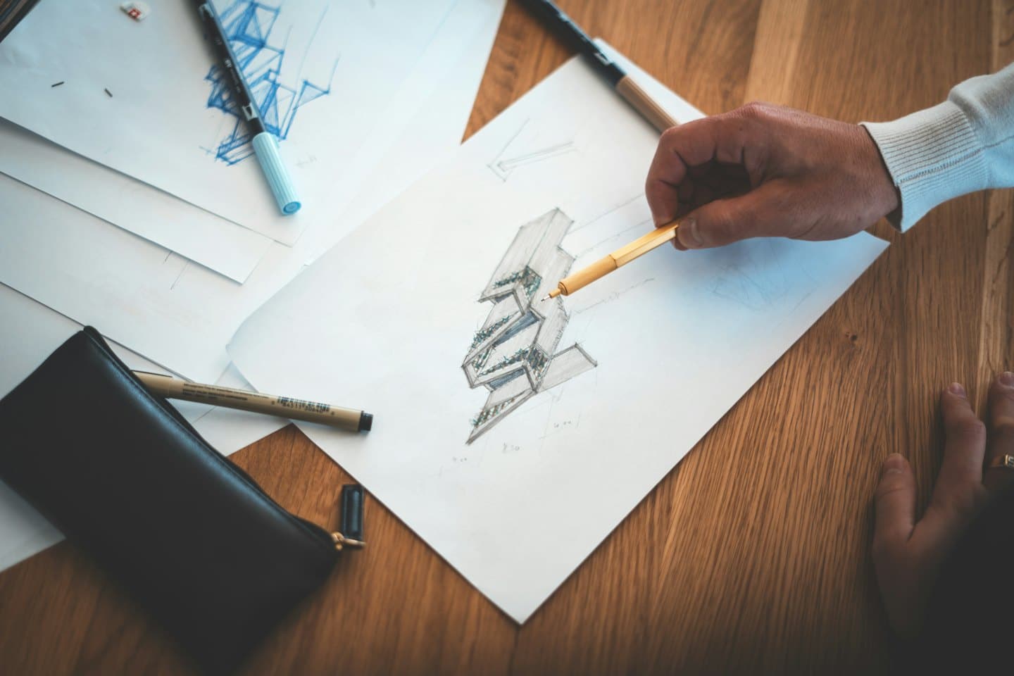 Hände, die mit einem orangefarbenen Stift architektonische Entwürfe auf weißem Papier skizzieren.